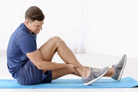 Man sitting on a yoga mat and holding his lower leg in pain