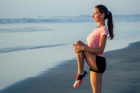 Woman doing a knee to chest stretch in the beach