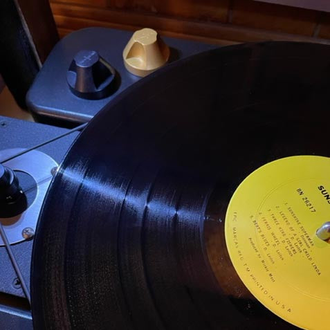 Vinyl record with yellow label on a turntable next to black and gold 45 adapters.