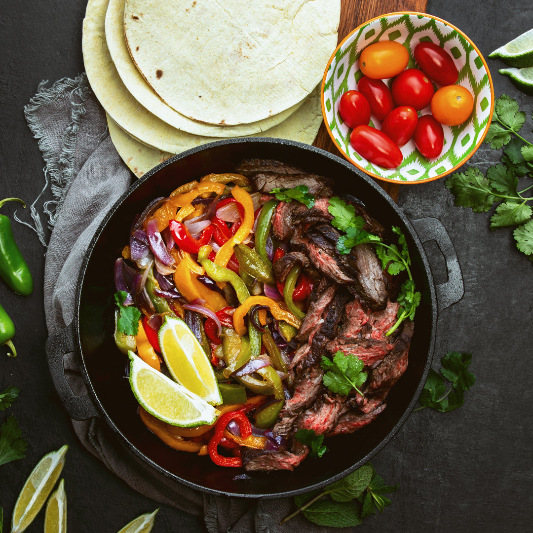tequila marinated steak fajitas in a cooking pan with taco tortilla and tomatoes in a bowl