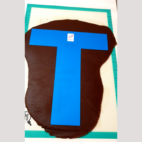 Image of letter T baking stencil on rolled out chocolate cookie dough