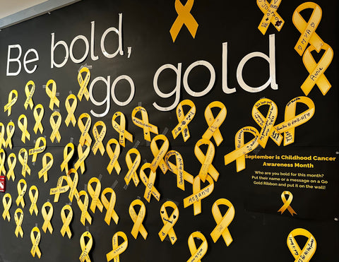 A board in the RMH-NY lobby says Be Bold. Go gold. with 30 or so golden ribbons pinned up all around on the wall.
