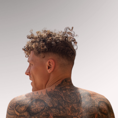 Man with tattoos that has curly hair demonstrating a drop fade hairstyle for men