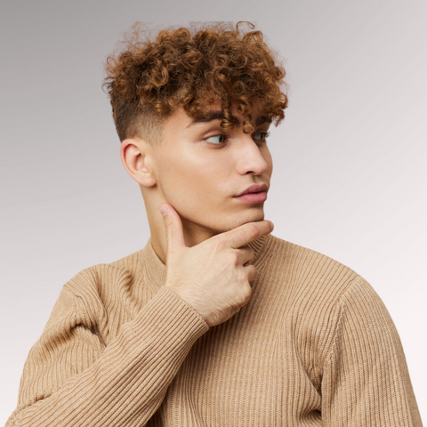 Man in a tan shirt with curly hair with a serious look on his face demonstrating a curly faux hawk hairstyle