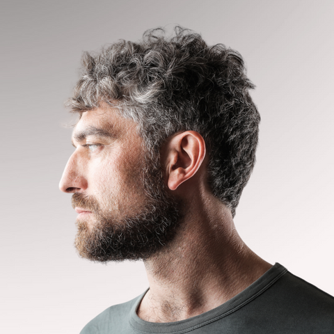 A man in a green shirt with grey hair demonstrating a wavy tousled forward hairstyle for men who have wavy, thinning hair