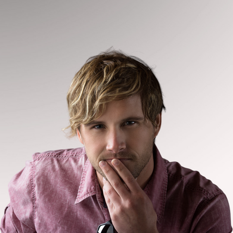 A man in a mauve shirt with blonde hair demonstrating a beachy waves hairstyle for men who have wavy, thinning hair