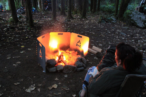 A hiker sitting in front of a campfire with fire reflector