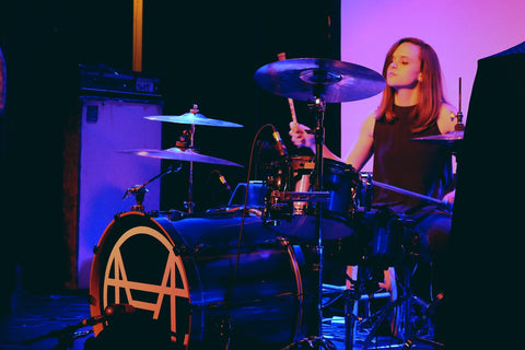 Chrissy sits behind a drum set on stage