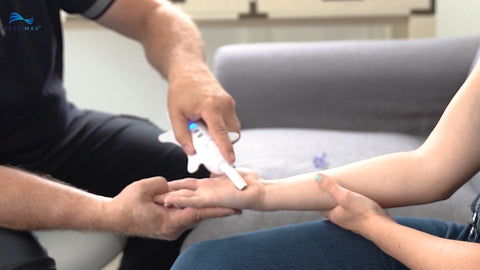 A practitioner is using the tip of the Rezzimax Tuner to draw an X in the palm of the patient's hand.