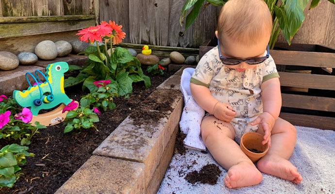 Chubby baby in little sunglasses, playing with a pot in a garden