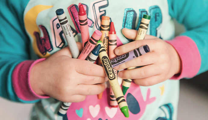 Child in colorful shirt holding a bundle of crayons.