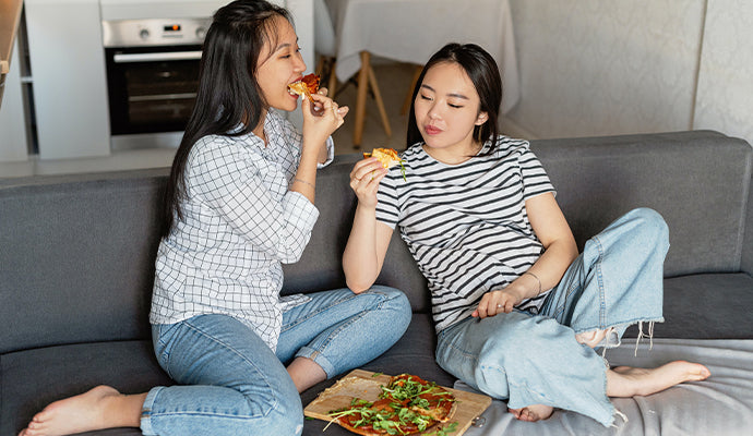 A woman eats pizza on the couch with her pregnant partner, yum!