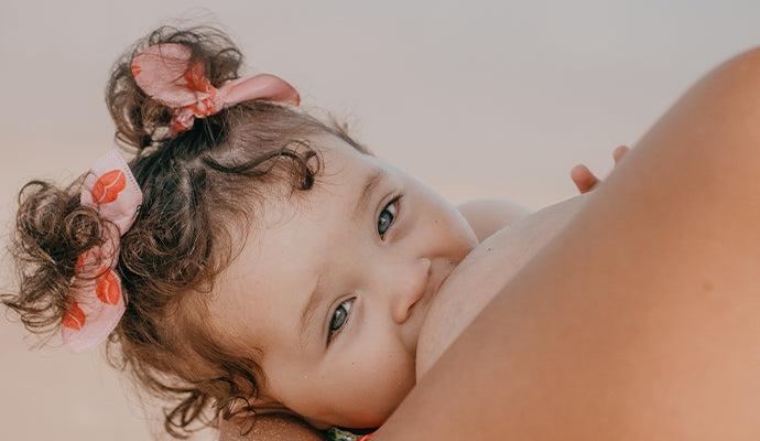 Baby girl with pink bows in her pigtails breastfeeds with her mom