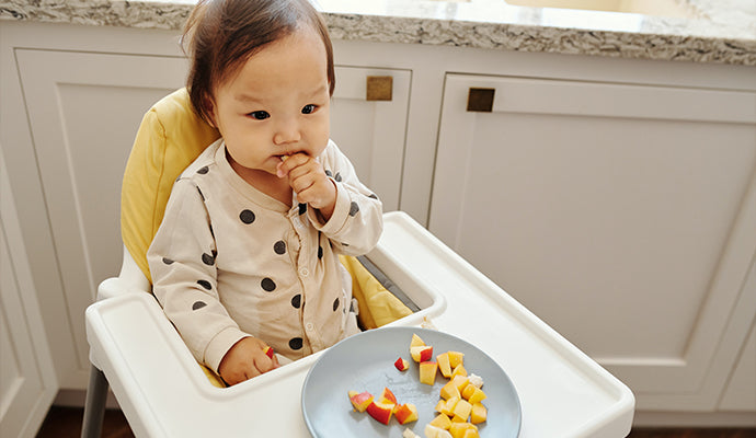 Baby sits in high chair and nibbles on chopped up pieces of apple and banana. Yum!