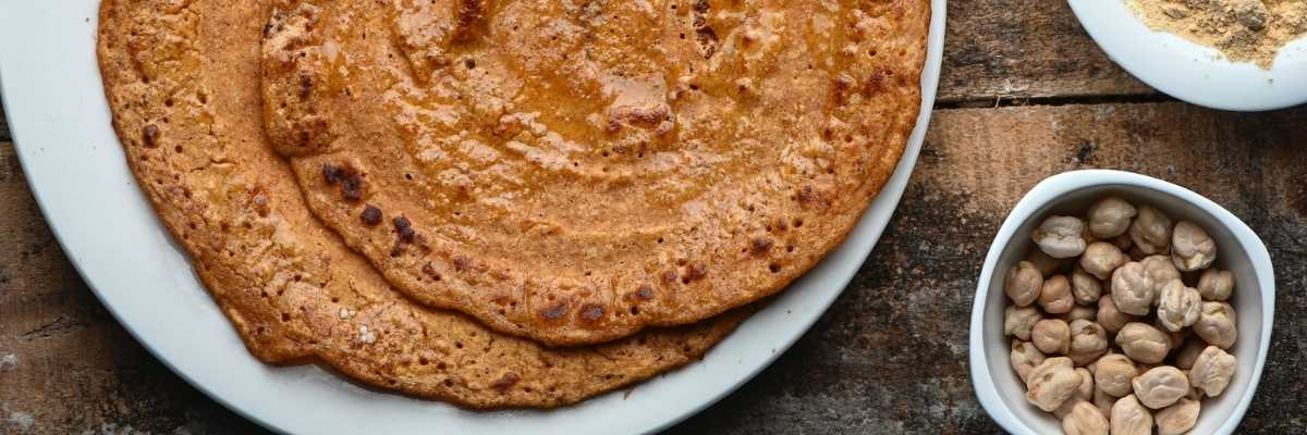 close up of dosa on a white plate with a small bowl of chickpeas