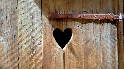 a wooden toilet door with a heart carved into it