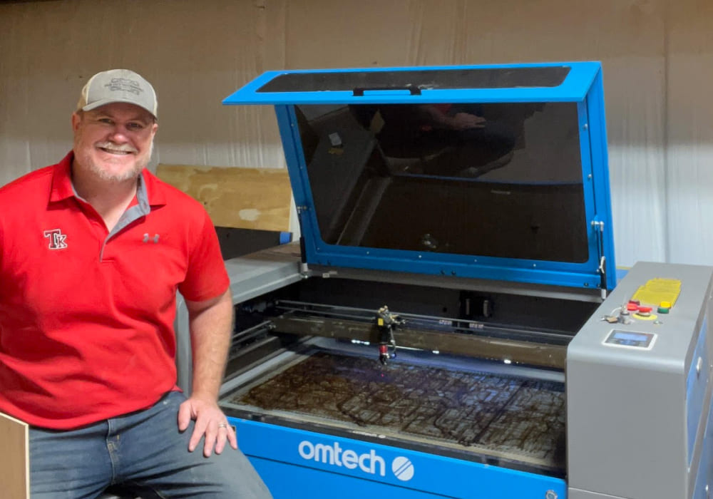 man sitting next to omtech laser engraving machine