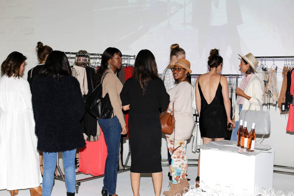 People crowded at the STL launch party looking over Sirah The Label clothing on coat racks.