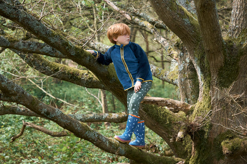 Boy climbing tree wearing Muddy Puddles parka and wellies