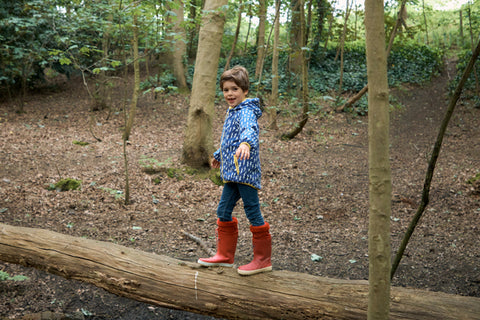 boy walking on log wearing muddy puddles waterproof jacket