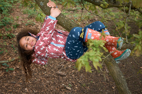 girl climbing tree wearing muddy puddles jacket