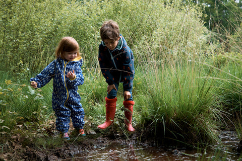 children playing in muddy puddle wearing waterproofs