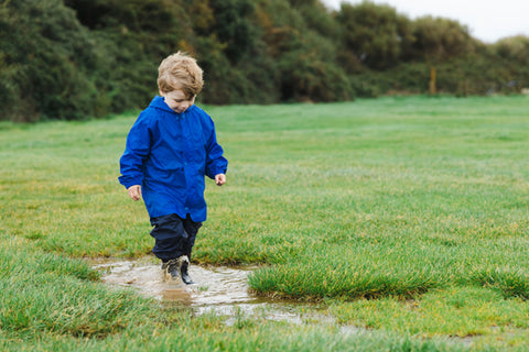 Boy splashing in puddle wearing Muddy Puddles waterproofs