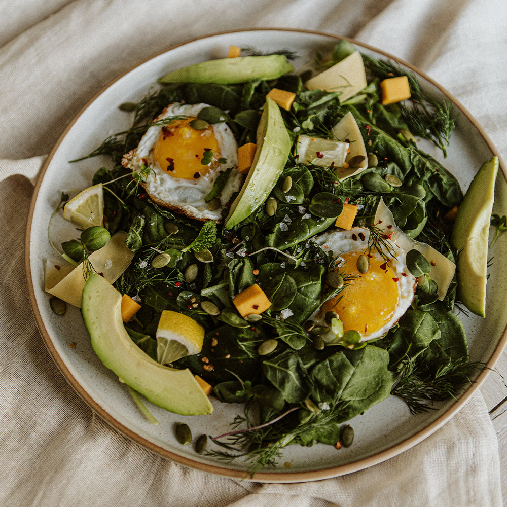 Salad on large white plate with avocado and eggs