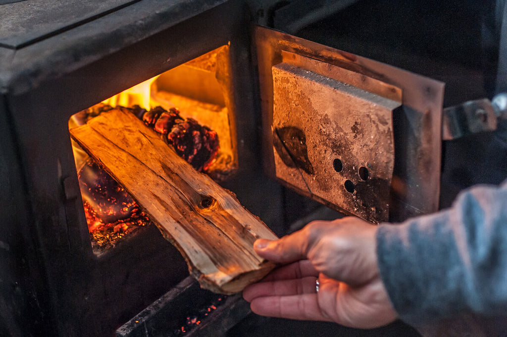 Modern wood stove: person putting a piece of wood in a wood-burning stove