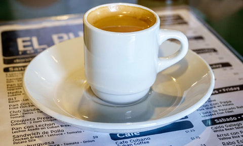 A cafecito sits on top of a menu in café