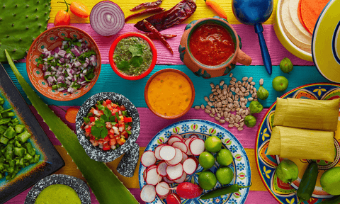 Colorful table with pots of guacamole, rice, beans, radishes, limes, tamales and salsas