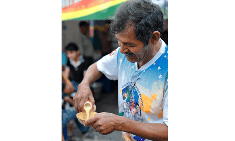 Un hombre vierte chicha en una taza de una botella pequeña