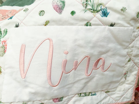 name embroidery on baby girl quilt that says "nina"