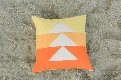 Orange and yellow quilted pillow cover on a beach