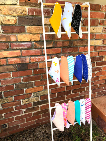Baby bibs hanging on blanket ladder leaning against exterior brick wall