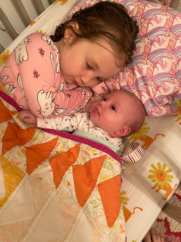 baby laying with big sister under handmade quilt