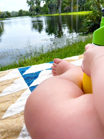 baby on handmade baby quilt on a picnic by the water