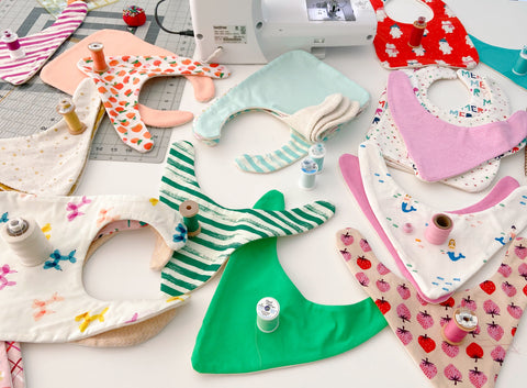 lots of baby bibs laid out on fabric cutting desk