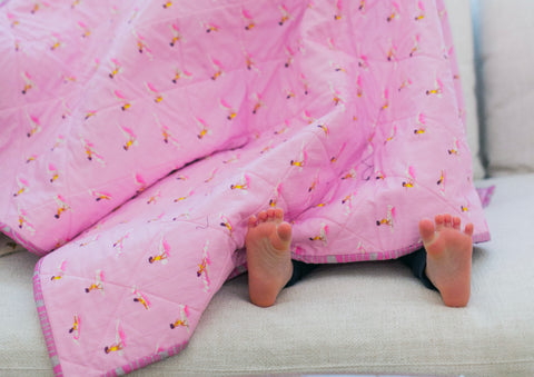 pink quilt with surfer girls and toddler feet poking out underneath