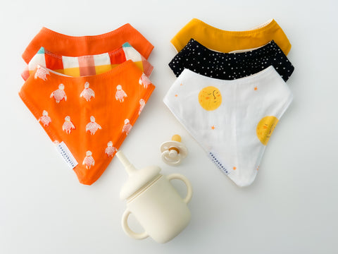 two sets of handmade, gender neutral baby bibs with a sippy cup and pacifier