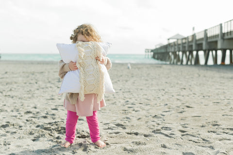 toddler girl holding quilted pillow with macrame on beach