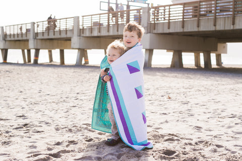 2 boys snuggled under baby size quilt on the beach