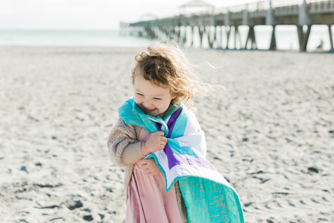 little girl wearing a happy quilt on the beach
