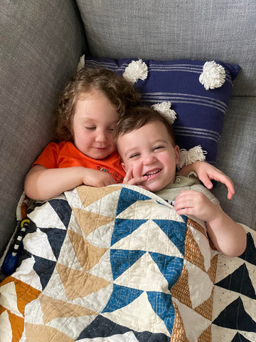two toddlers laying under custom quilt