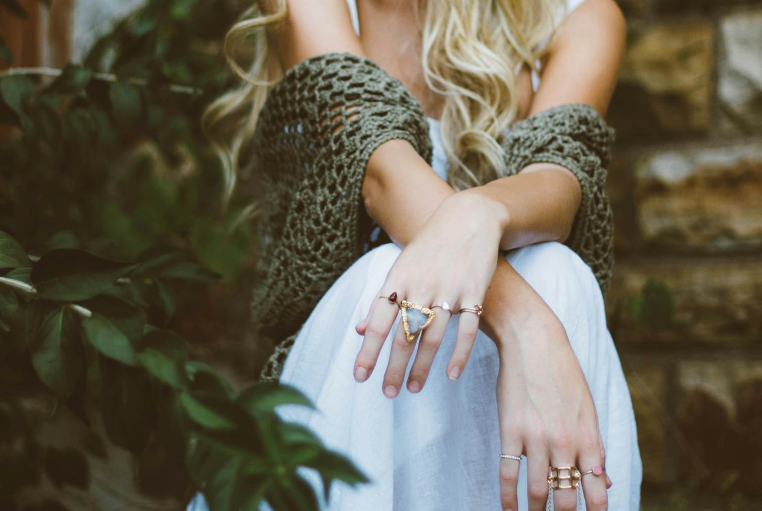 Woman sits down wearing a white dress, green shawl, and gold rings