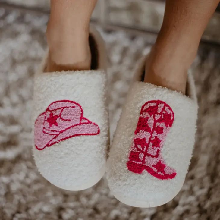 A pair of pink and white slippers with a cowgirl hat and cowgirl boots.