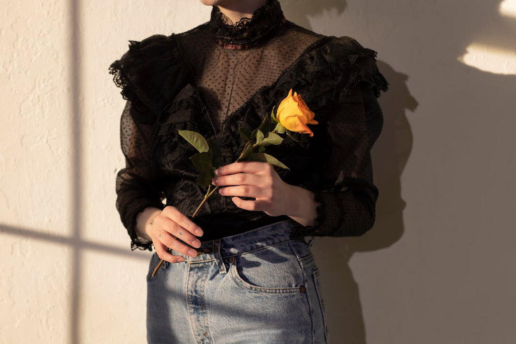 Woman wearing jeans with boutique blouse and holding a yellow rose