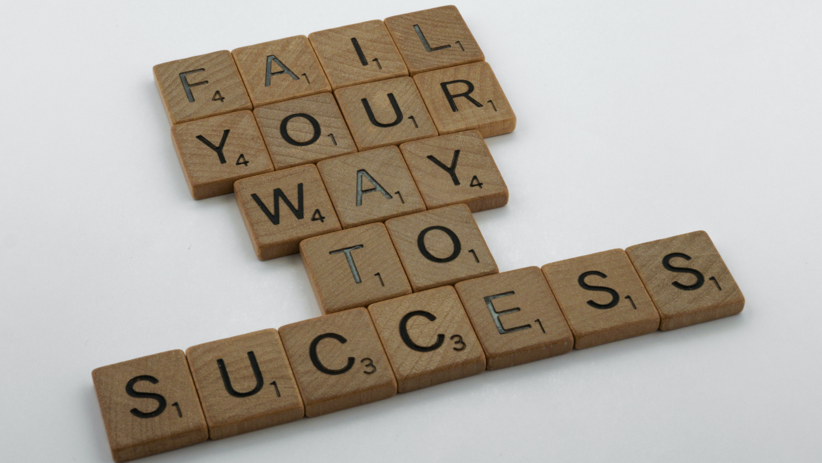 Scrabble tiles have been laid out on a white surface to read fail your way to success.