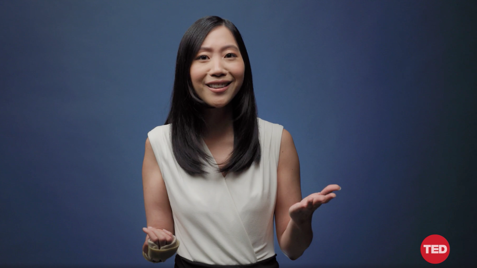 Disability activist Tiffany Yu, an Asian woman with medium length black hair stands in front of a dark grey background. She's wearing a cream-coloured blouse and has a tan wrist brace on her right hand. She's smiling looking at the camera.
