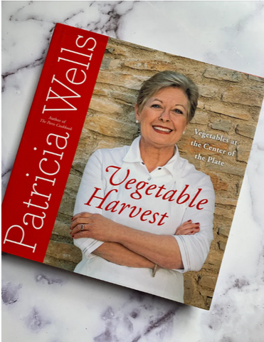 Patricia Wells crossing her arms and smiling.  She is wearing a white shirt.  The cover has a big red bar on the left for the title of the cookbook.